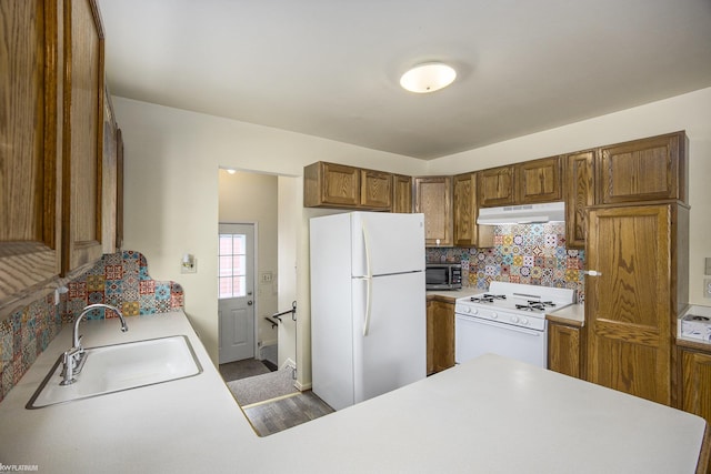 kitchen featuring sink, backsplash, white appliances, and kitchen peninsula