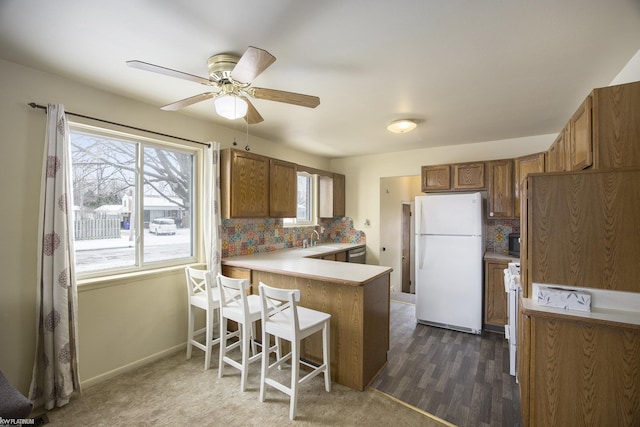 kitchen with a breakfast bar area, dark hardwood / wood-style flooring, decorative backsplash, kitchen peninsula, and white appliances