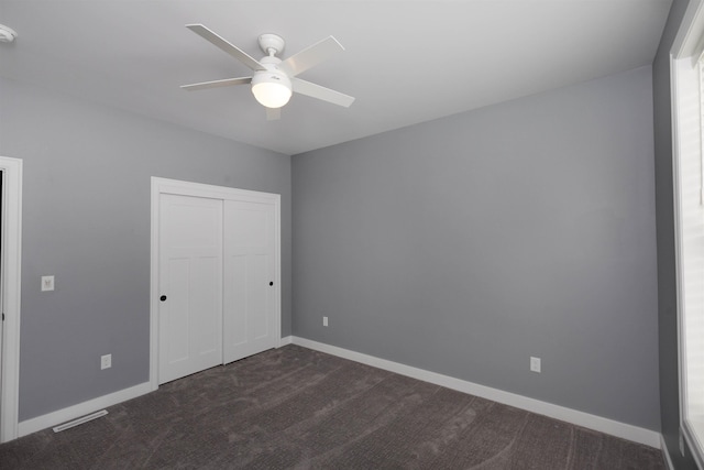 unfurnished bedroom with dark carpet, a closet, and ceiling fan