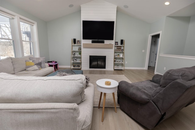 living room with a large fireplace, lofted ceiling, and light hardwood / wood-style flooring