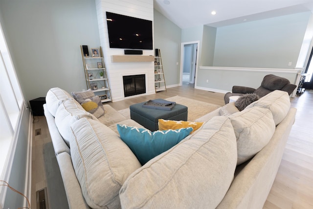 living room featuring lofted ceiling, a large fireplace, and light wood-type flooring