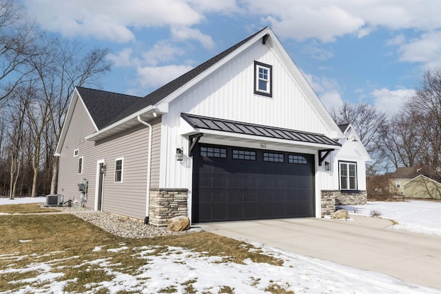 snow covered property featuring cooling unit and a garage