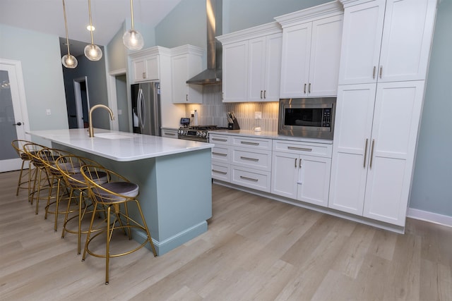 kitchen with appliances with stainless steel finishes, an island with sink, sink, white cabinets, and wall chimney range hood