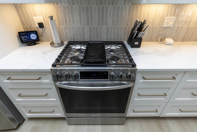 kitchen featuring light stone counters, stainless steel range with gas cooktop, decorative backsplash, and white cabinets