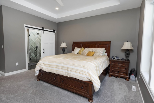 carpeted bedroom with ensuite bathroom, a barn door, and a tray ceiling