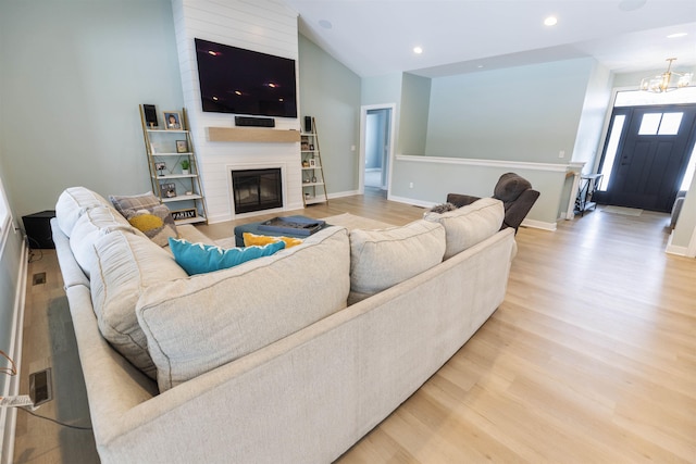 living room featuring a notable chandelier, a fireplace, vaulted ceiling, and light wood-type flooring