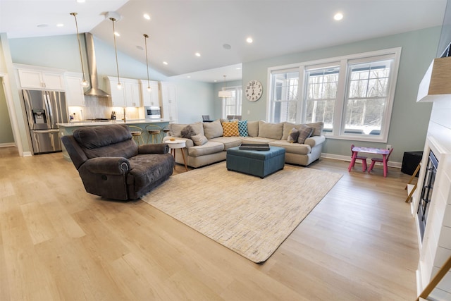 living room with high vaulted ceiling, plenty of natural light, and light hardwood / wood-style floors