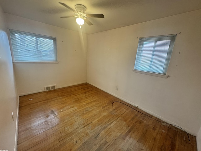 empty room featuring hardwood / wood-style floors, baseboards, visible vents, and ceiling fan