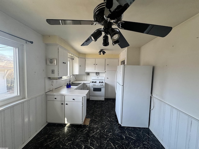 kitchen with a sink, white appliances, wainscoting, and light countertops