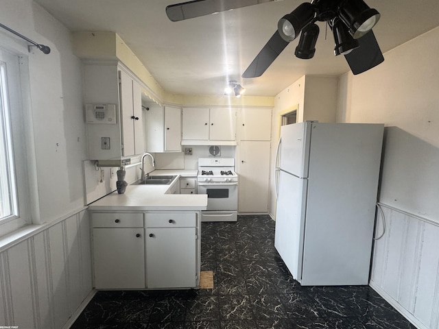 kitchen with white appliances, a wainscoted wall, a sink, light countertops, and white cabinets