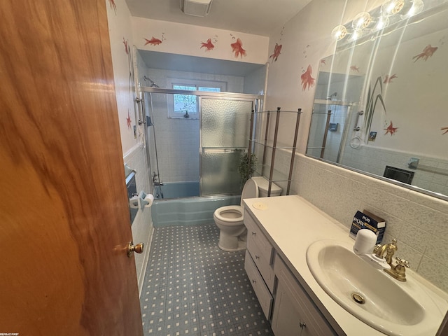 bathroom featuring bath / shower combo with glass door, toilet, tile walls, and vanity