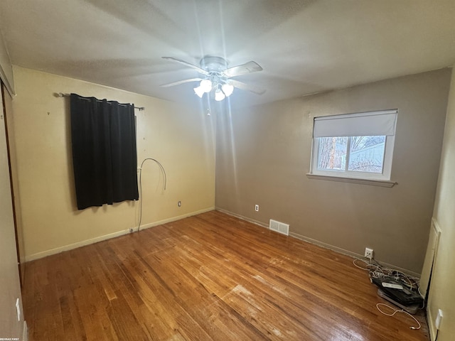 empty room with a ceiling fan, wood finished floors, visible vents, and baseboards