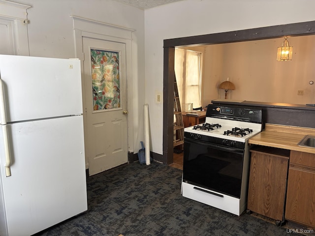 kitchen featuring pendant lighting, range with gas stovetop, dark carpet, and white fridge