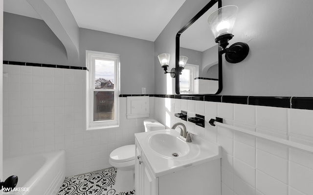 bathroom with tile walls, a tub to relax in, tile patterned flooring, vanity, and toilet