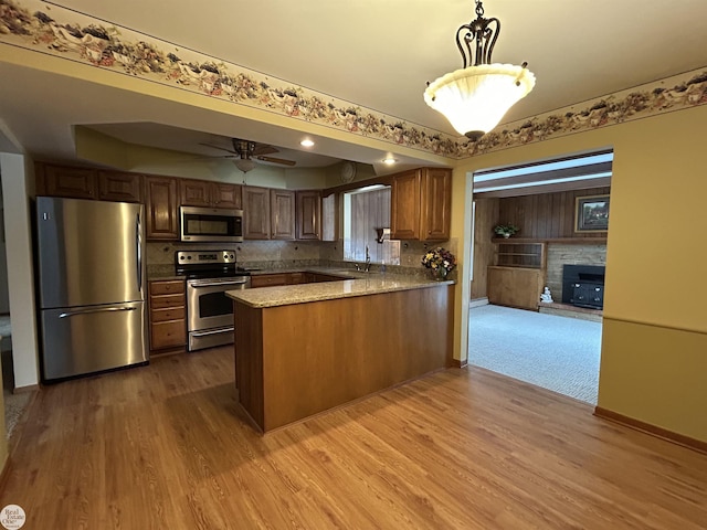 kitchen featuring sink, hanging light fixtures, kitchen peninsula, stainless steel appliances, and light wood-type flooring