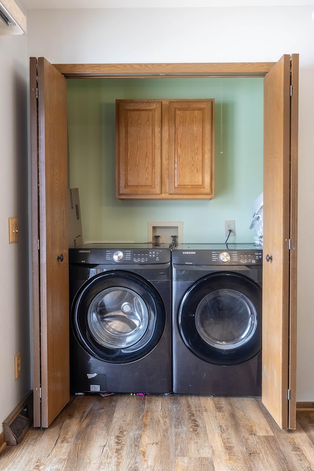 clothes washing area with cabinets, separate washer and dryer, and light wood-type flooring