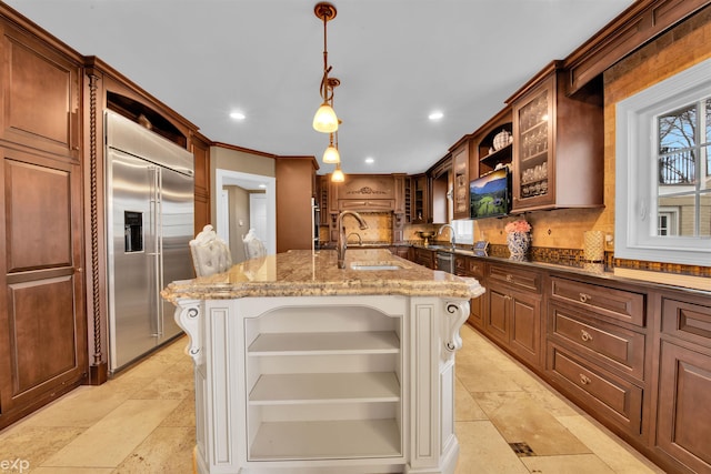 kitchen with a kitchen island with sink, sink, pendant lighting, and stainless steel built in refrigerator