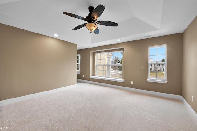 empty room featuring ceiling fan, a raised ceiling, and light carpet