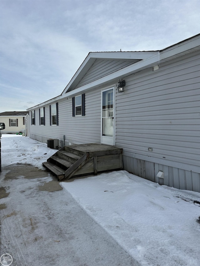 snow covered rear of property featuring central AC unit