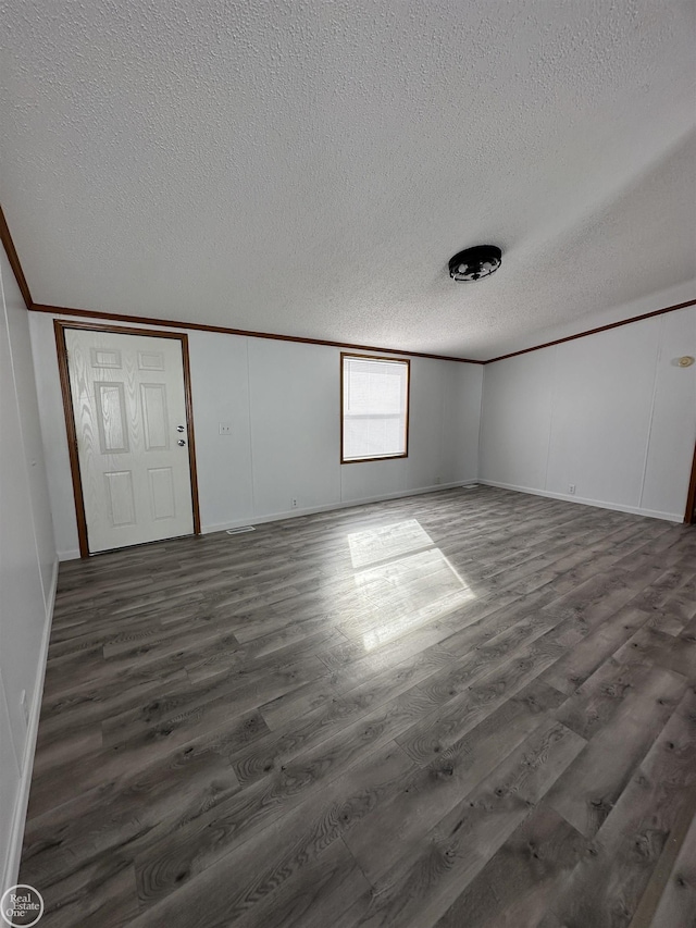 unfurnished room featuring dark wood-type flooring, ornamental molding, and a textured ceiling