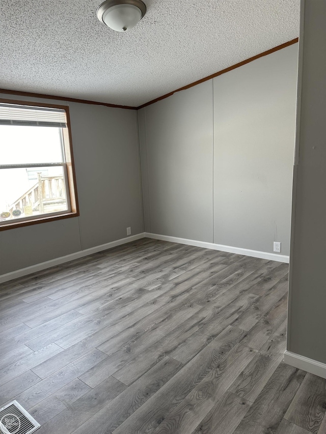 unfurnished room with hardwood / wood-style flooring, ornamental molding, and a textured ceiling