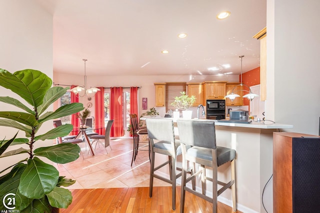 kitchen with kitchen peninsula, light brown cabinetry, decorative light fixtures, a kitchen bar, and black appliances