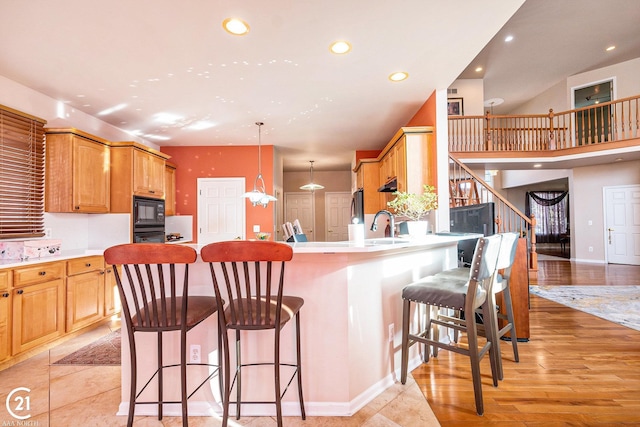 kitchen featuring a breakfast bar, decorative light fixtures, black appliances, kitchen peninsula, and light wood-type flooring