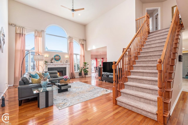 living room with a high ceiling, wood-type flooring, ceiling fan with notable chandelier, and a fireplace