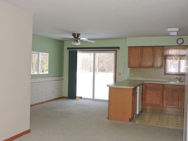 kitchen with kitchen peninsula, sink, light colored carpet, white dishwasher, and ceiling fan