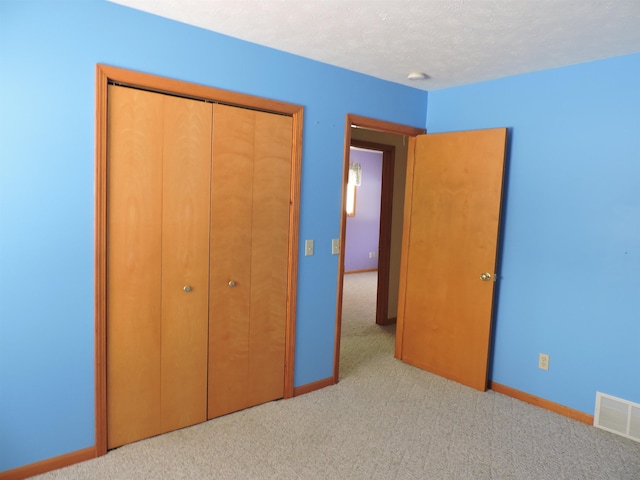 unfurnished bedroom featuring light carpet, a textured ceiling, and a closet