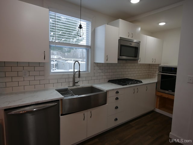 kitchen with sink, white cabinetry, pendant lighting, stainless steel appliances, and light stone countertops