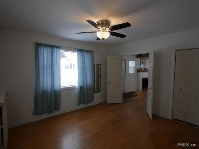 unfurnished bedroom with hardwood / wood-style flooring, ceiling fan, a fireplace, and multiple windows