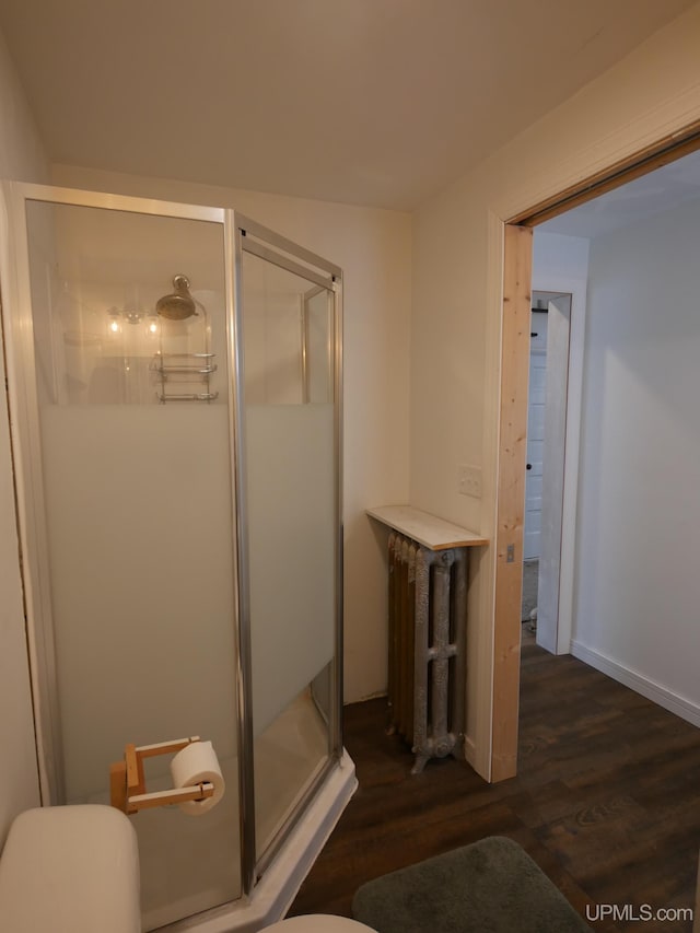 bathroom with radiator heating unit, a shower with door, and wood-type flooring