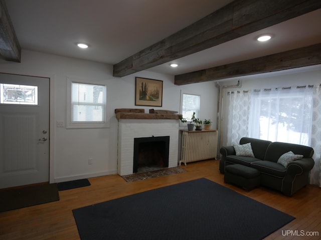 living room featuring radiator, hardwood / wood-style flooring, beamed ceiling, and a brick fireplace