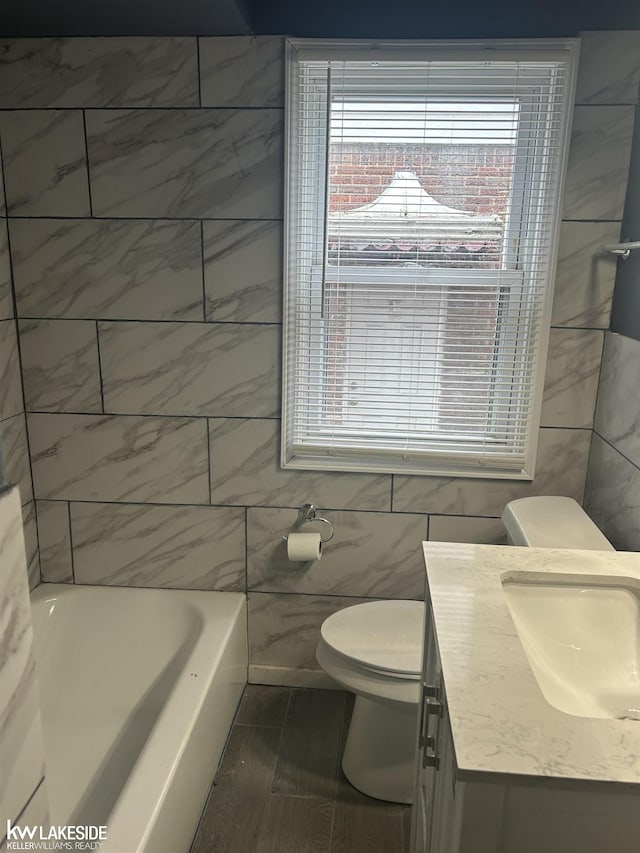 bathroom with vanity, a bathtub, tile walls, and toilet