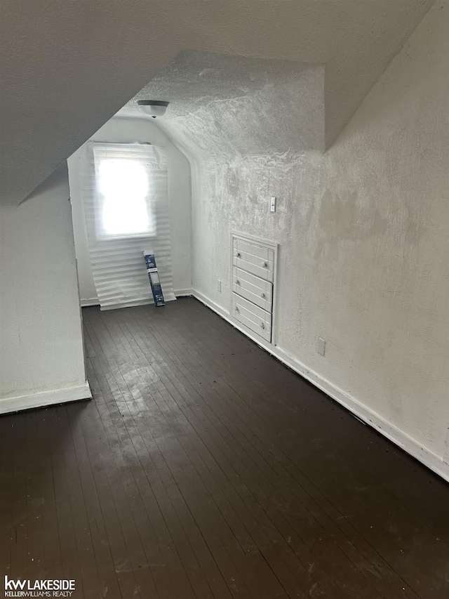 additional living space featuring lofted ceiling, dark hardwood / wood-style floors, and a textured ceiling