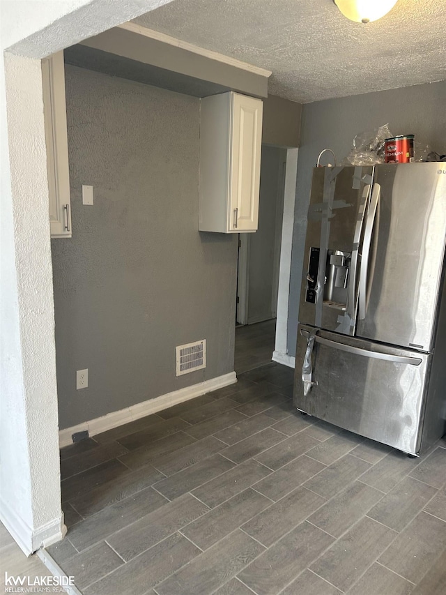 kitchen featuring stainless steel refrigerator with ice dispenser, a textured ceiling, and white cabinets