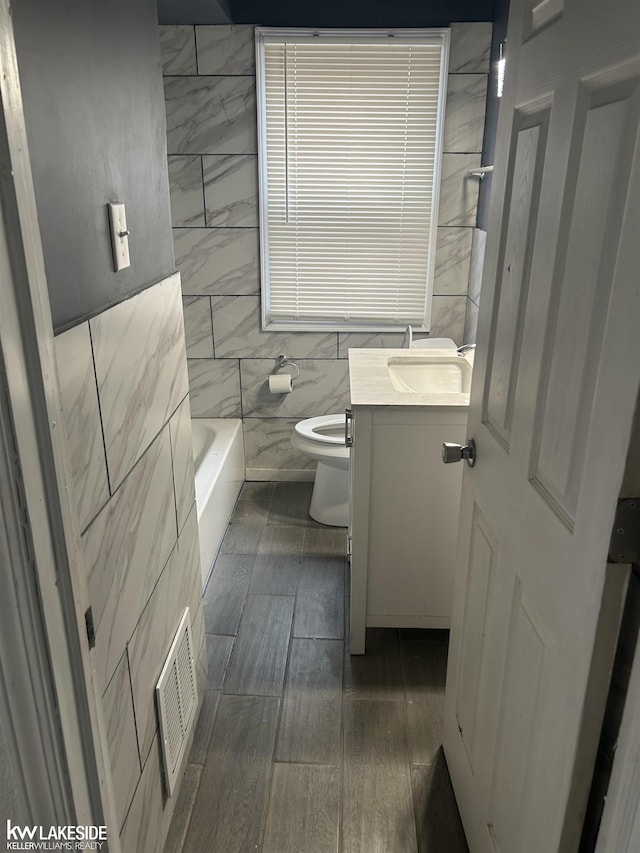 bathroom with toilet, tile walls, vanity, a tub, and hardwood / wood-style floors