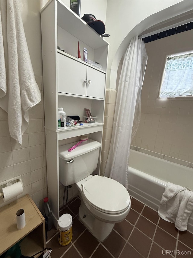 bathroom featuring shower / bathtub combination with curtain, tile patterned floors, toilet, and tile walls