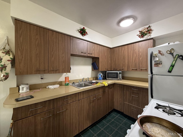 kitchen with sink, white appliances, dark brown cabinets, and dark tile patterned floors