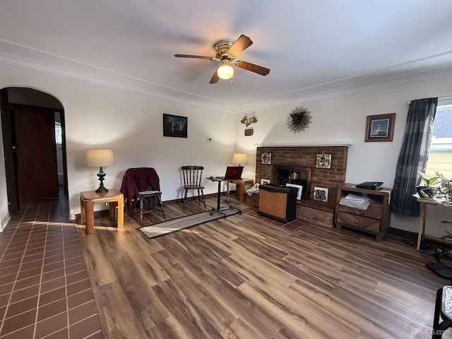 sitting room with dark hardwood / wood-style flooring, a brick fireplace, crown molding, and ceiling fan