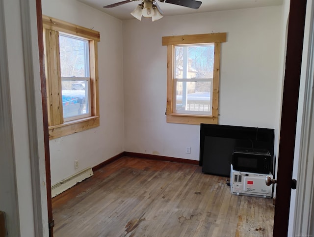 empty room featuring a baseboard heating unit, plenty of natural light, hardwood / wood-style floors, and ceiling fan