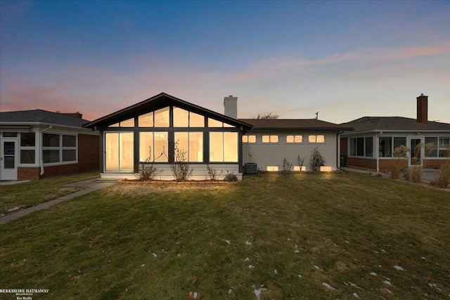 back house at dusk with central AC unit, a yard, and a sunroom