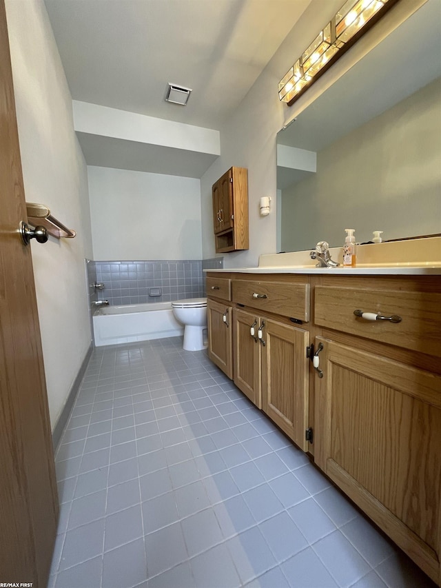 bathroom featuring tiled tub, vanity, tile patterned floors, and toilet