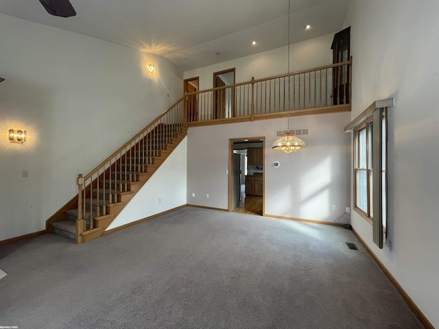 unfurnished living room with carpet, a chandelier, and a high ceiling