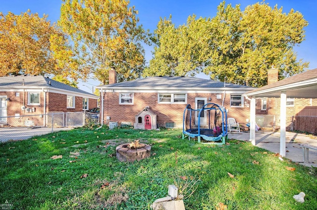 rear view of house with a trampoline, a fire pit, and a lawn