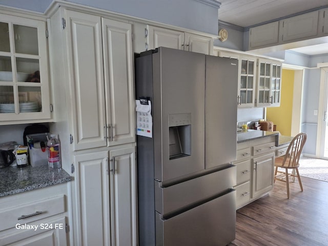 kitchen with dark wood-type flooring, stainless steel refrigerator with ice dispenser, built in desk, white cabinets, and dark stone counters