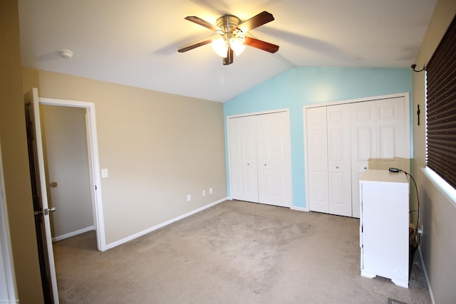 unfurnished bedroom featuring multiple closets, light colored carpet, lofted ceiling, and ceiling fan