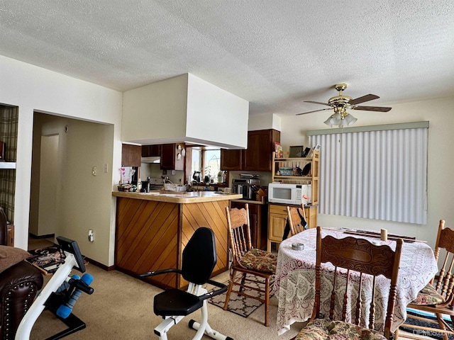 kitchen featuring a textured ceiling, ceiling fan, white microwave, light carpet, and a peninsula