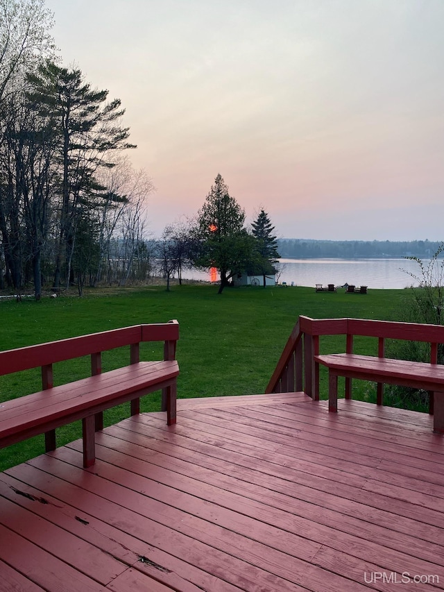 deck at dusk featuring a yard and a water view